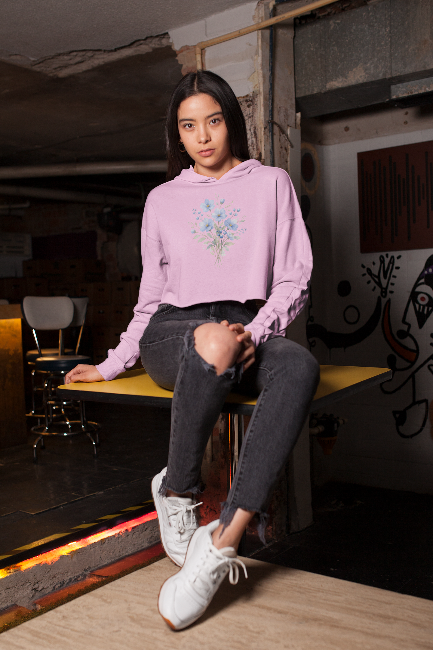 Woman wearing a light pink hoodie with floral design sitting on a bench in an urban setting.
