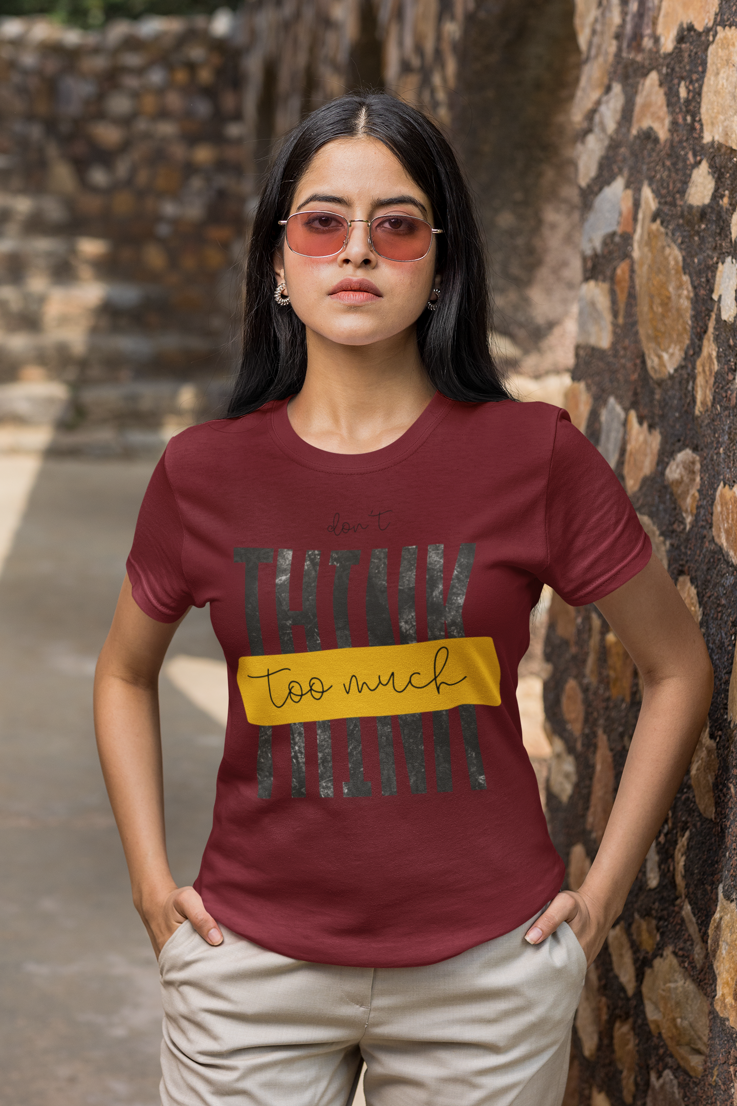 Woman wearing a Maroon t-shirt with text standing against a stone wall.