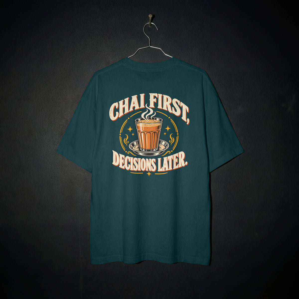 Petrol Blue Chai First Decisions Later oversized T-shirt on a hanger against a dark backdrop, front view of the cutting chai graphic print