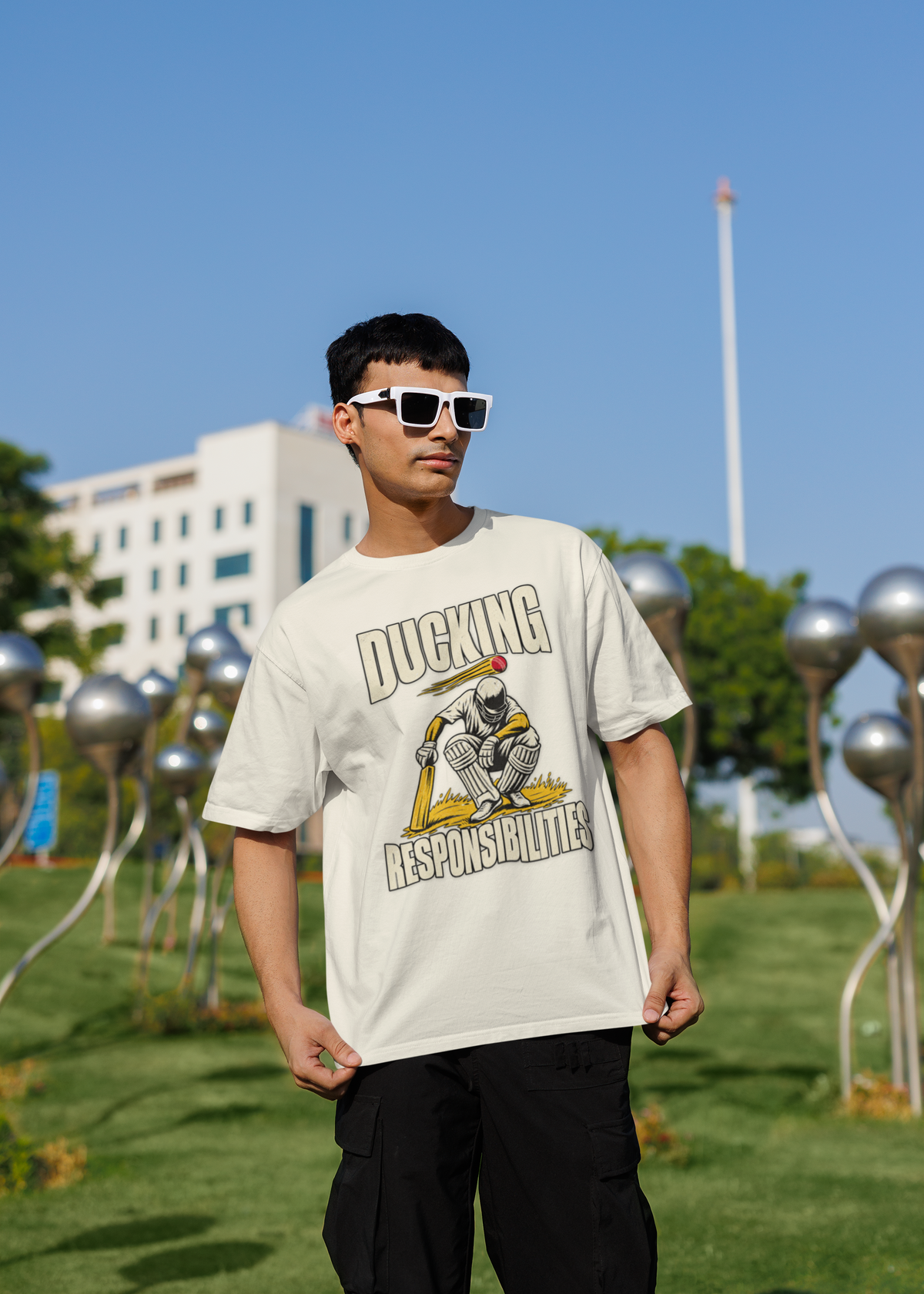 Man wearing the off white Ducking Responsibilities oversized cricket T-shirt with black cargo trousers and white sunglasses, outdoors
