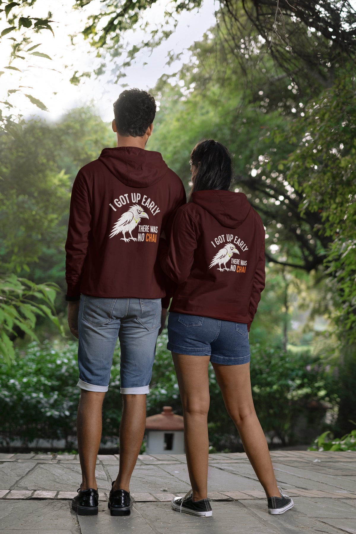 Maroon unisex hoodie with white crow and no chai slogan back print, worn by a couple seen from behind