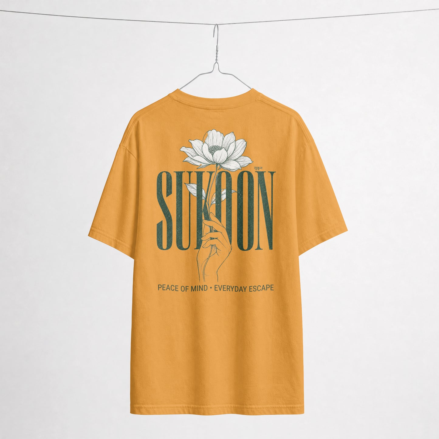 Nauma Sukoon oversized t-shirt in golden yellow on a hanger, back print with lotus flower and hand illustration