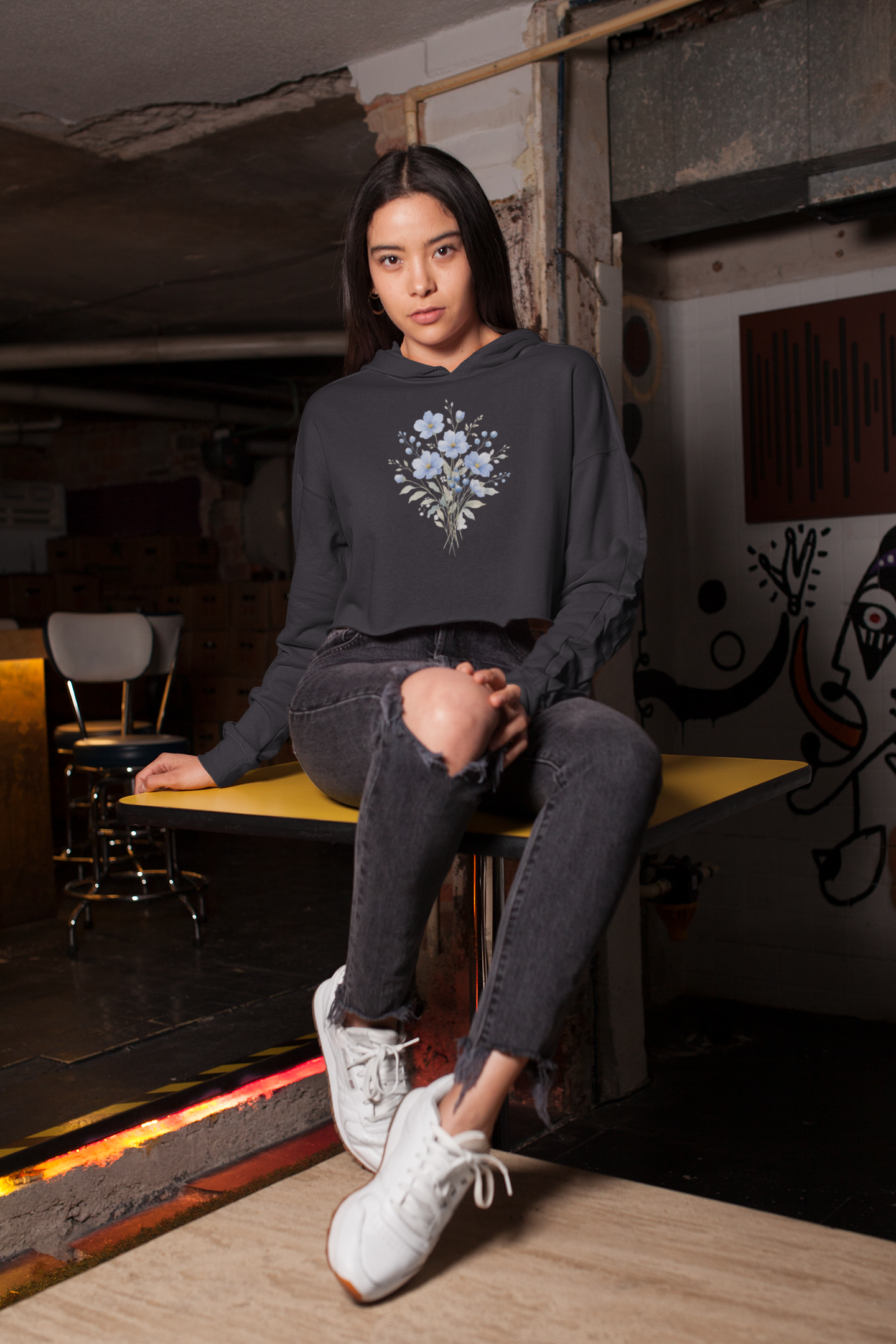 Woman wearing a black hoodie with floral design sitting on a bench in an urban setting.