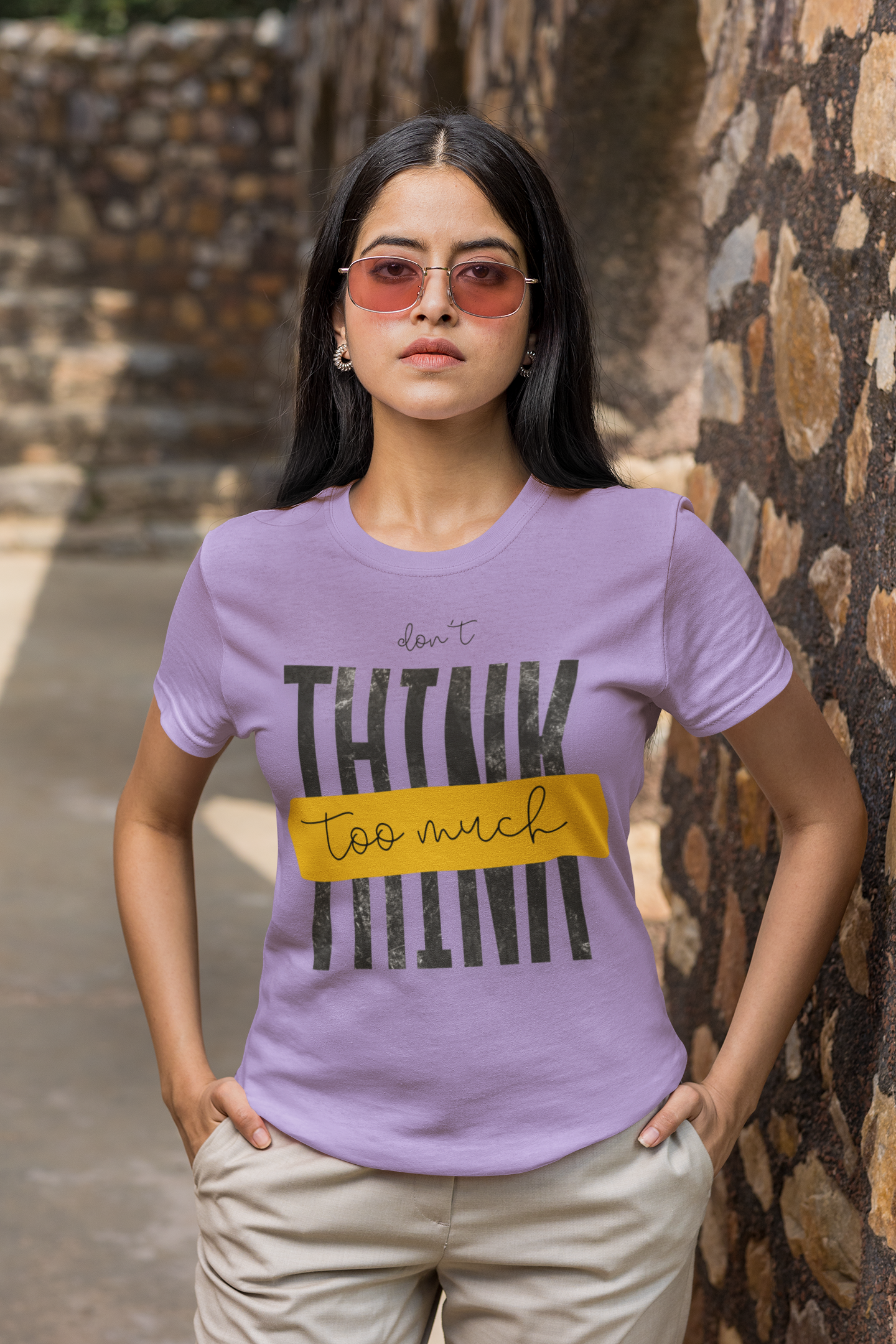 Woman wearing a Lavender t-shirt with text standing against a stone wall.