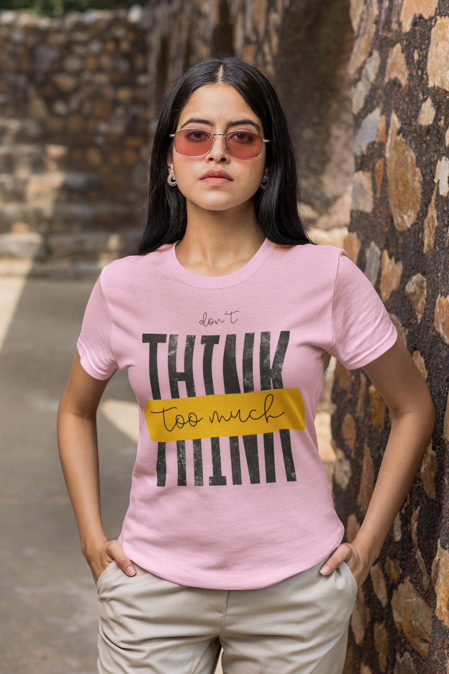 Woman wearing a Light Pink t-shirt with text standing against a stone wall.