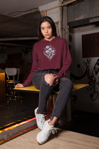 Woman wearing a maroon hoodie with floral design sitting on a bench in an urban setting.