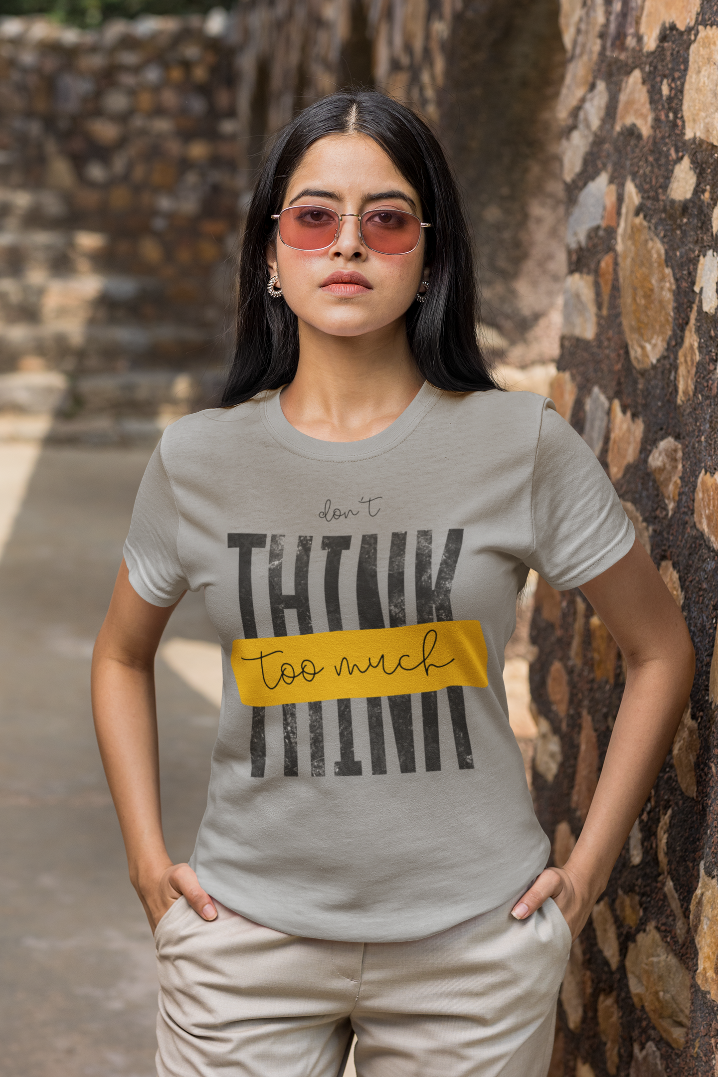 Woman wearing a Melange Grey t-shirt with text standing against a stone wall.