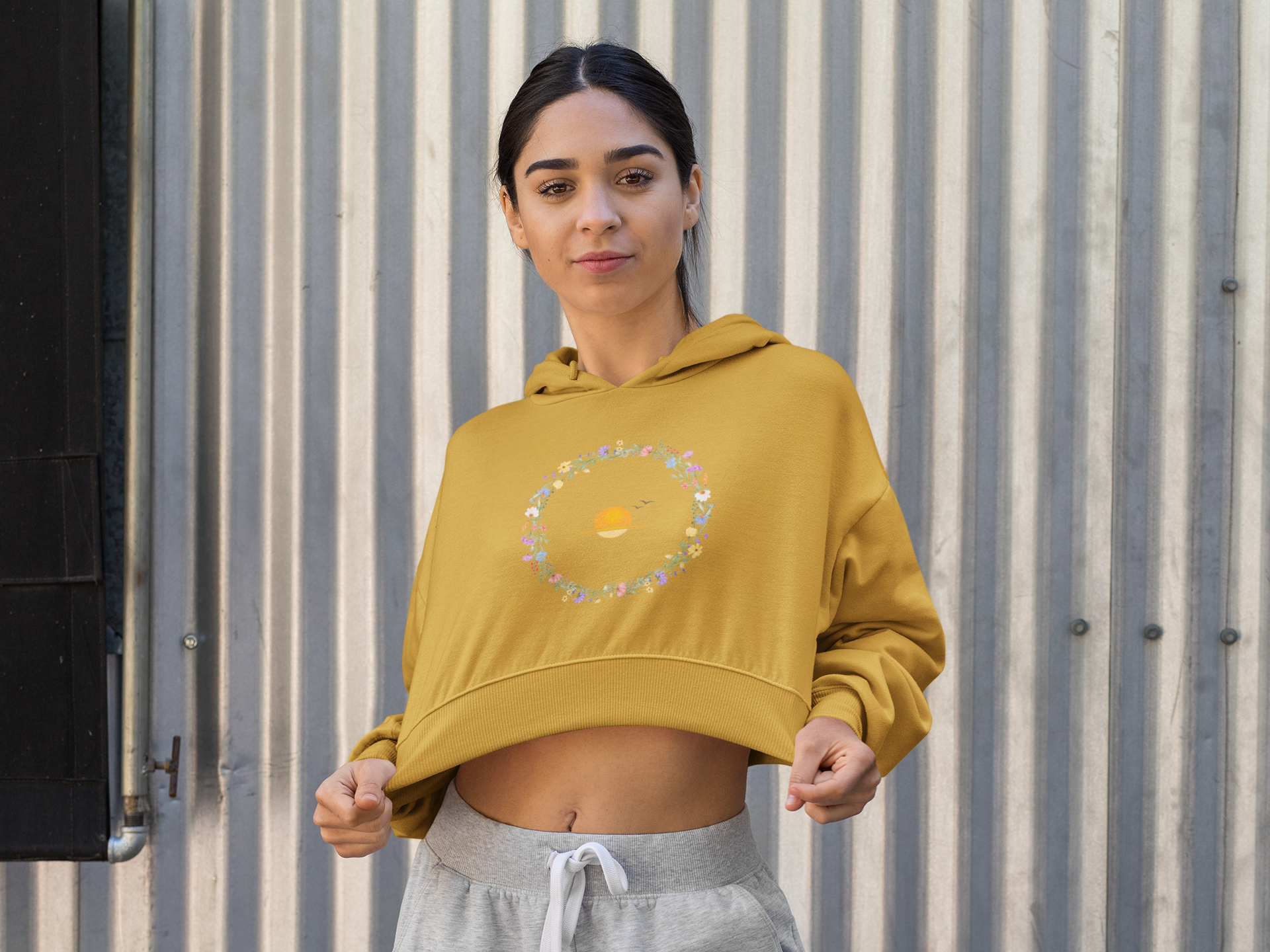 Mustard Yellow Woman wearing a mustard yellow hoodie with a circular design against a corrugated metal background