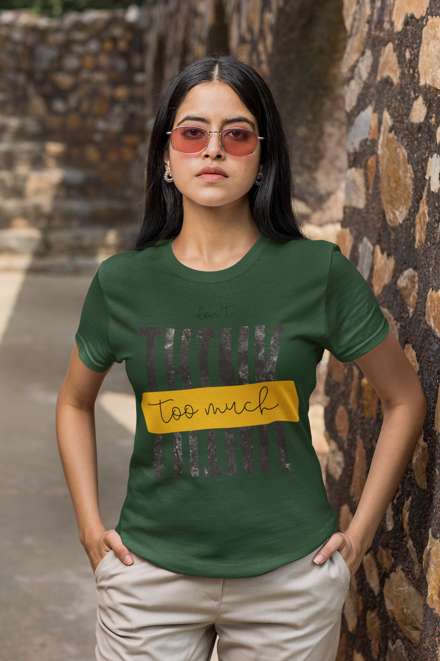 Woman wearing a Olive Green t-shirt with text standing against a stone wall.