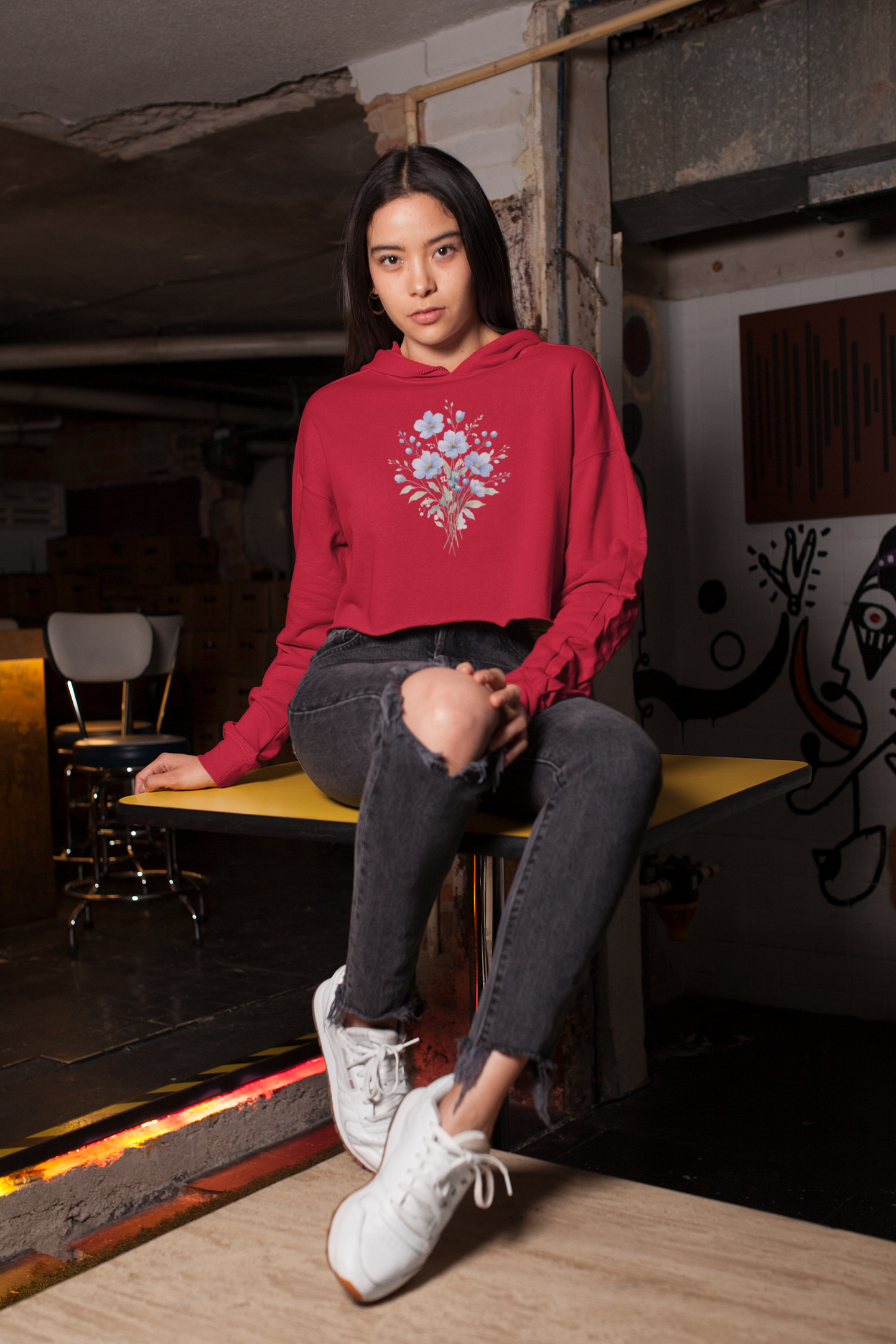 Woman wearing a red hoodie with floral design sitting on a bench in an urban setting.