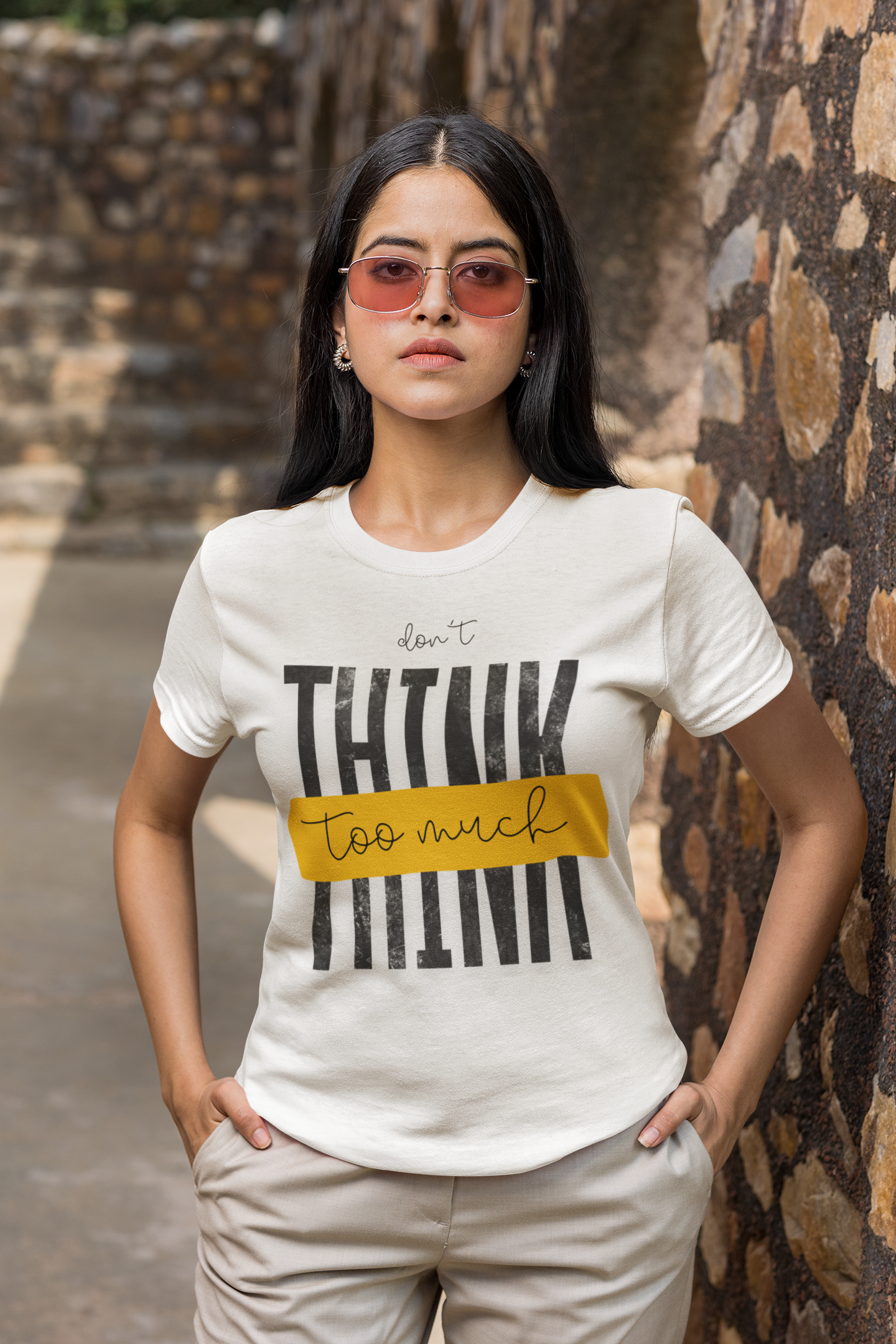 Woman wearing a White t-shirt with text standing against a stone wall.