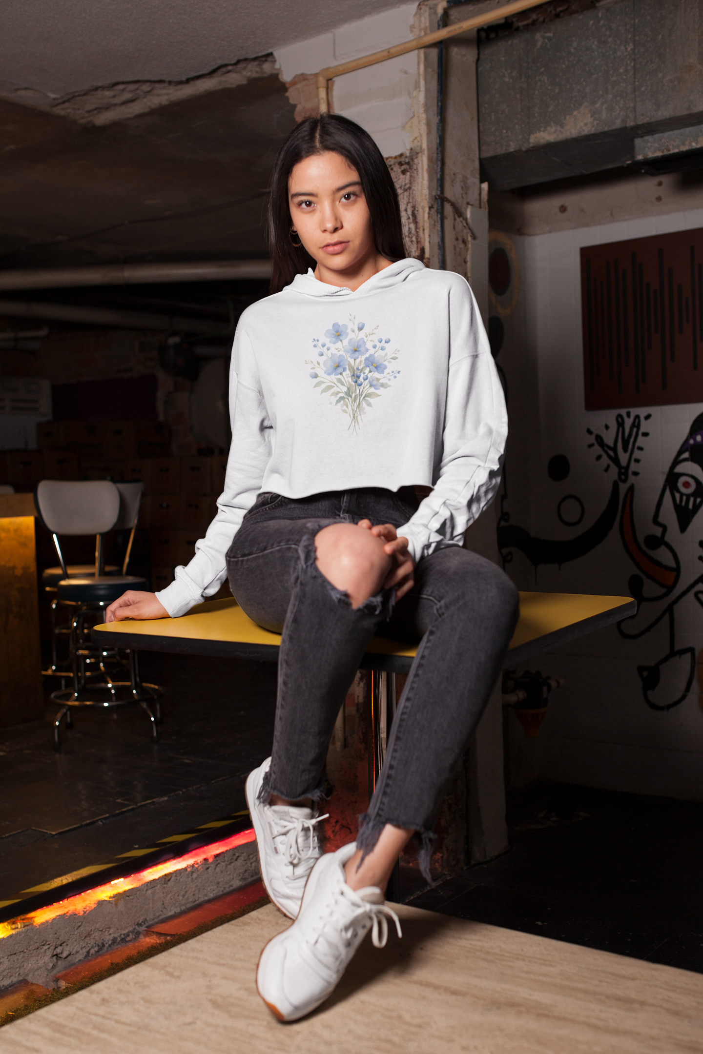 Woman wearing a white hoodie with floral design sitting on a bench in an urban setting.