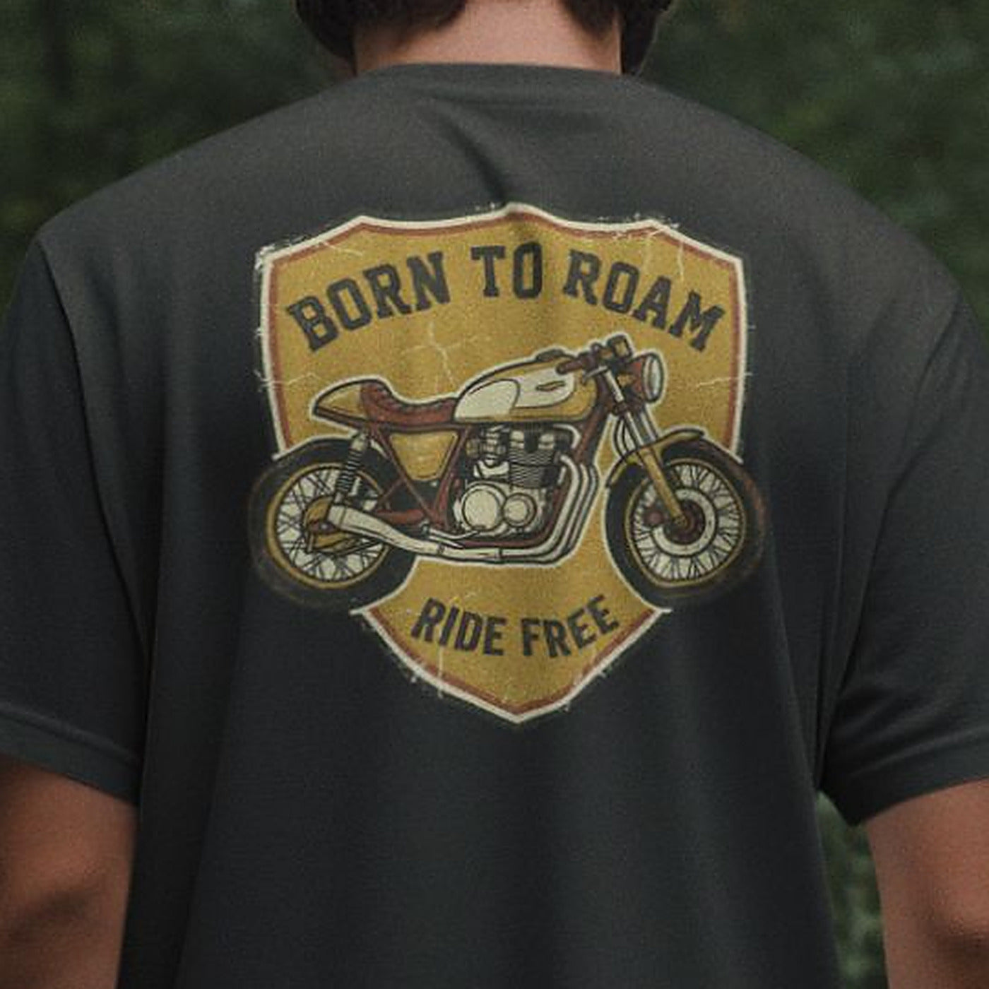 Close-up of the Born To Roam back print on a black oversized t-shirt, showing the distressed mustard shield badge and vintage cafe racer motorcycle artwork