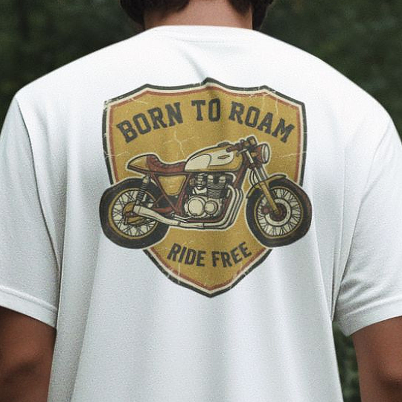 Close-up of the Born To Roam cafe racer badge on a white oversized t-shirt, showing the Ride Free banner and cracked vintage print texture