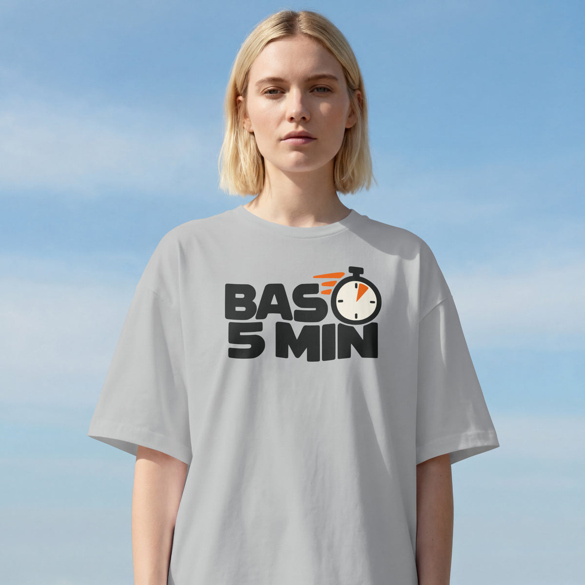 Woman with a blonde bob wearing the Melange Grey Bas 5 Min oversized t-shirt against a blue sky, front print visible