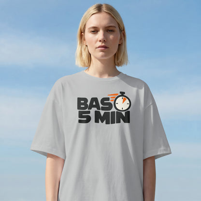 Woman with a blonde bob wearing the Melange Grey Bas 5 Min oversized t-shirt against a blue sky, front print visible