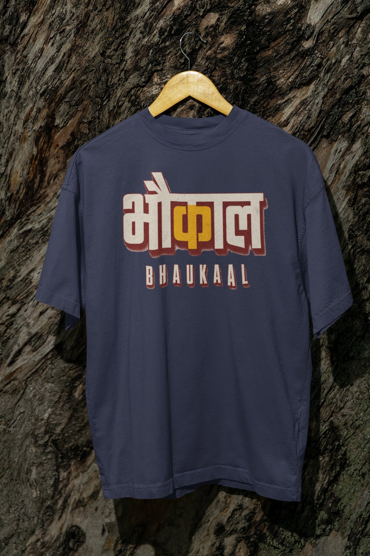 Navy Blue Bhaukaal oversized t-shirt on a hanger against a textured bark wall, showing the full 3D Hindi typography front print
