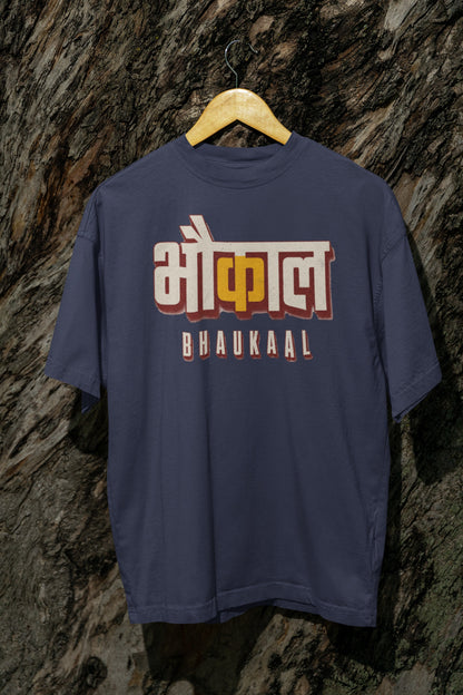 Navy Blue Bhaukaal oversized t-shirt on a hanger against a textured bark wall, showing the full 3D Hindi typography front print