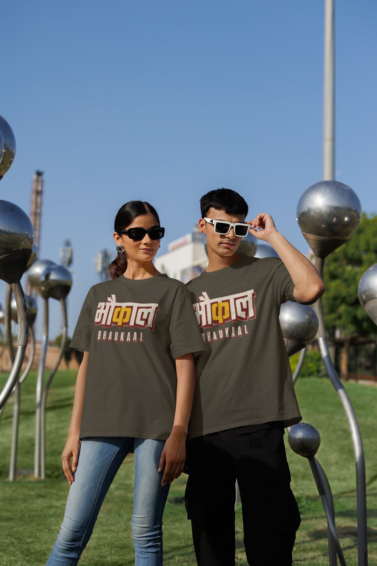 Olive Green Bhaukaal oversized t-shirt worn by a man and a woman outdoors, Hindi typography print across the chest