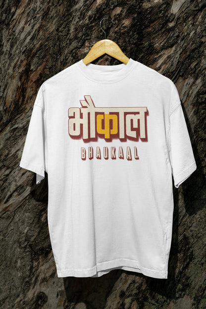 White Bhaukaal oversized t-shirt on a hanger against a textured bark wall, showing the full 3D Hindi typography front print