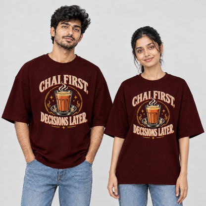 Maroon Chai First Decisions Later unisex oversized T-shirt worn by a man and a woman, front print with a cutting chai glass and retro cream lettering