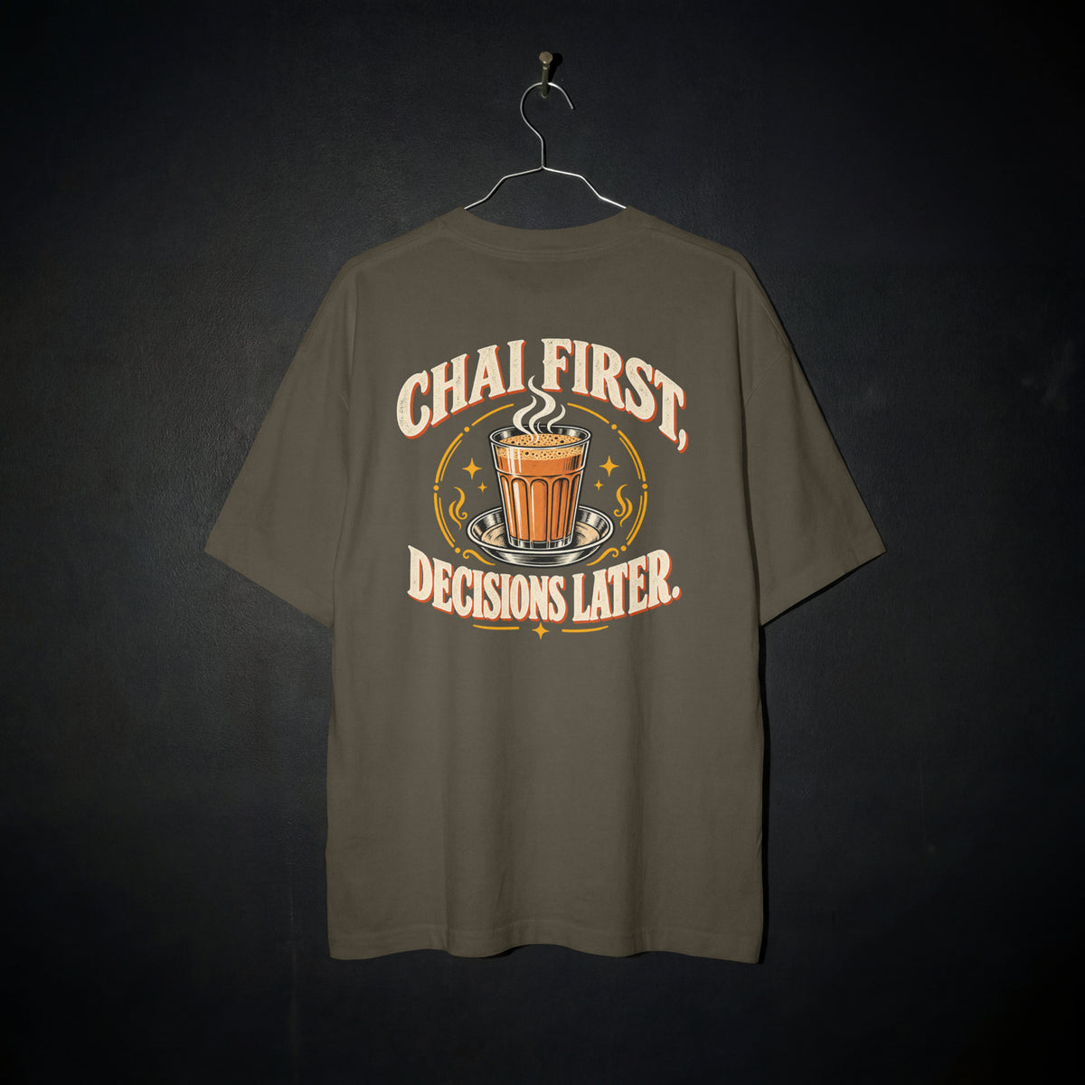 Olive Green Chai First Decisions Later oversized T-shirt on a hanger against a dark backdrop, front view of the cutting chai graphic print