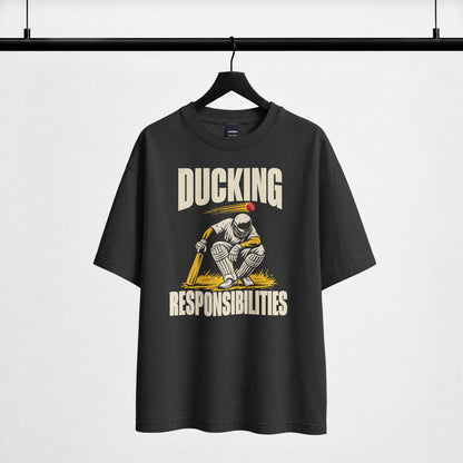 Black Ducking Responsibilities oversized T-shirt on a hanger, front print of a helmeted cricket batter ducking a red ball