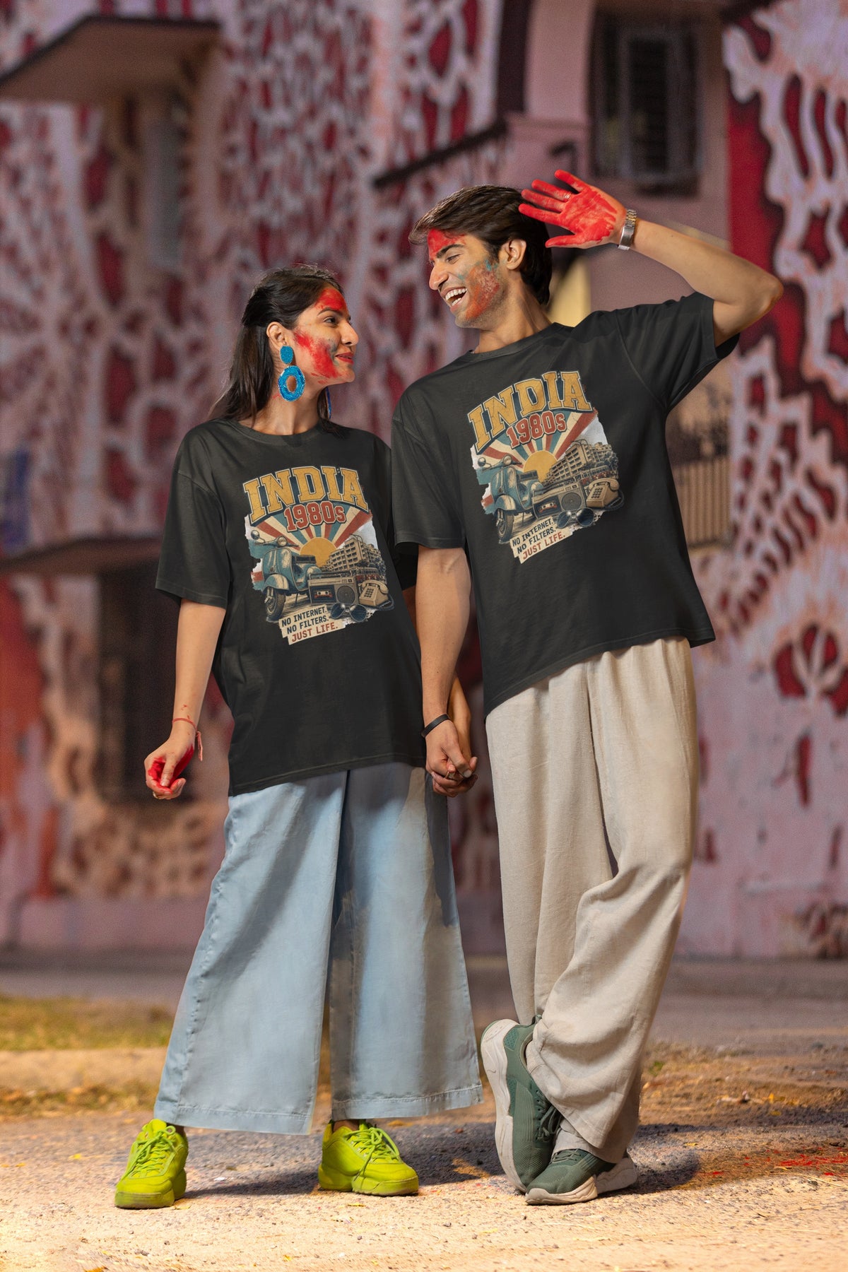 Man and woman wearing the Nauma India 80s retro oversized t-shirt in Black against a patterned pink wall