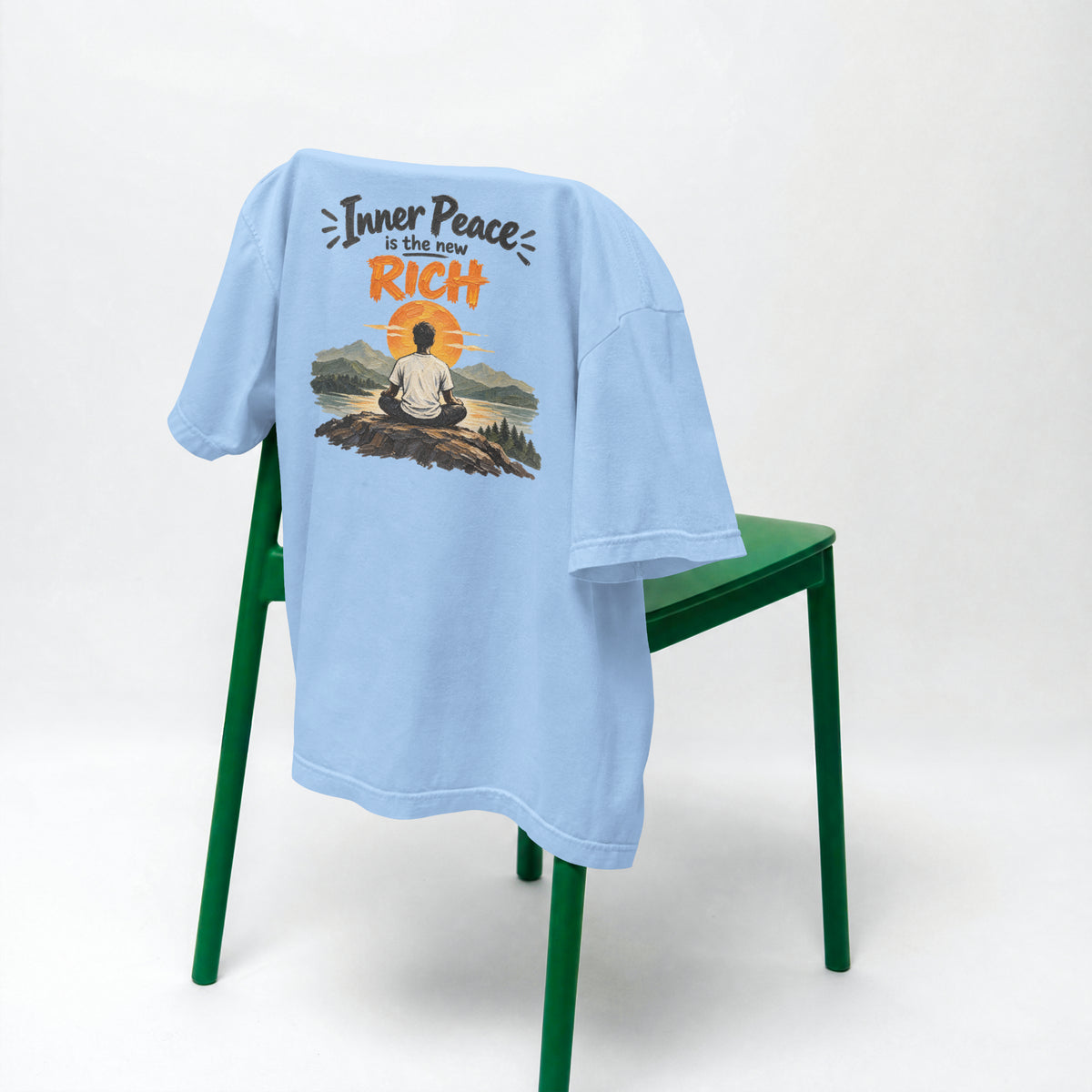 Baby Blue Inner Peace Is The New Rich oversized t-shirt draped over a green chair, showing the front print