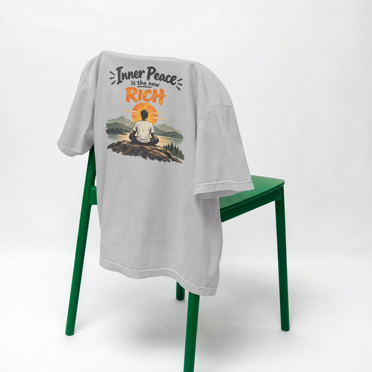 Melange Grey Inner Peace Is The New Rich oversized t-shirt draped over a green chair, showing the front print