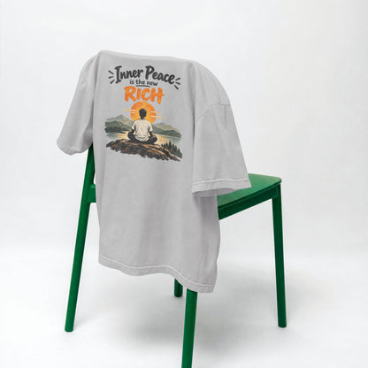 Melange Grey Inner Peace Is The New Rich oversized t-shirt draped over a green chair, showing the front print