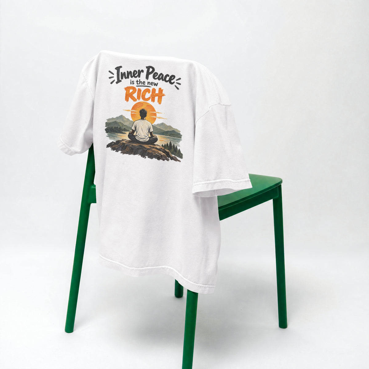 White Inner Peace Is The New Rich oversized t-shirt draped over a green chair, showing the front print