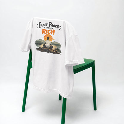 White Inner Peace Is The New Rich oversized t-shirt draped over a green chair, showing the front print