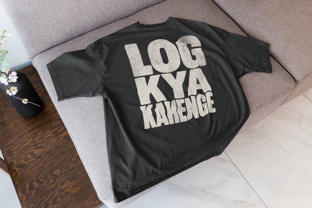 Black Log Kya Kahenge oversized t-shirt laid flat on a sofa, showing the stacked distressed cream lettering front print