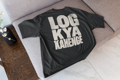 Black Log Kya Kahenge oversized t-shirt laid flat on a sofa, showing the stacked distressed cream lettering front print