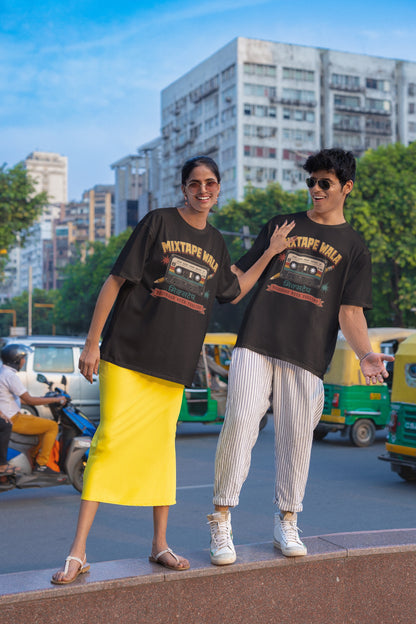 Man and woman wearing the Black Mixtape Wala oversized t-shirt on a city street with auto-rickshaws