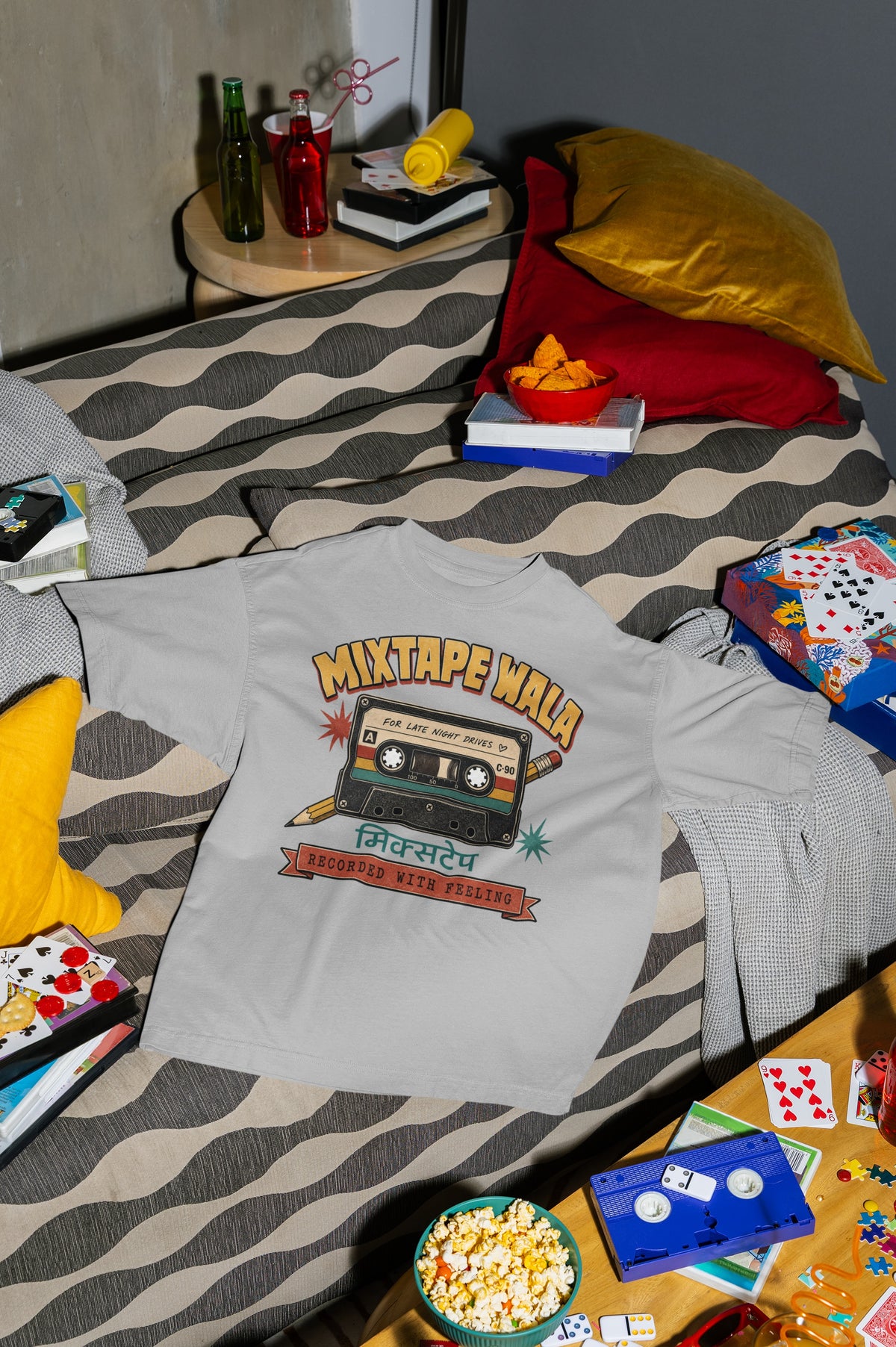 Melange Grey Mixtape Wala oversized t-shirt laid flat on a bed with cushions, cassette and popcorn