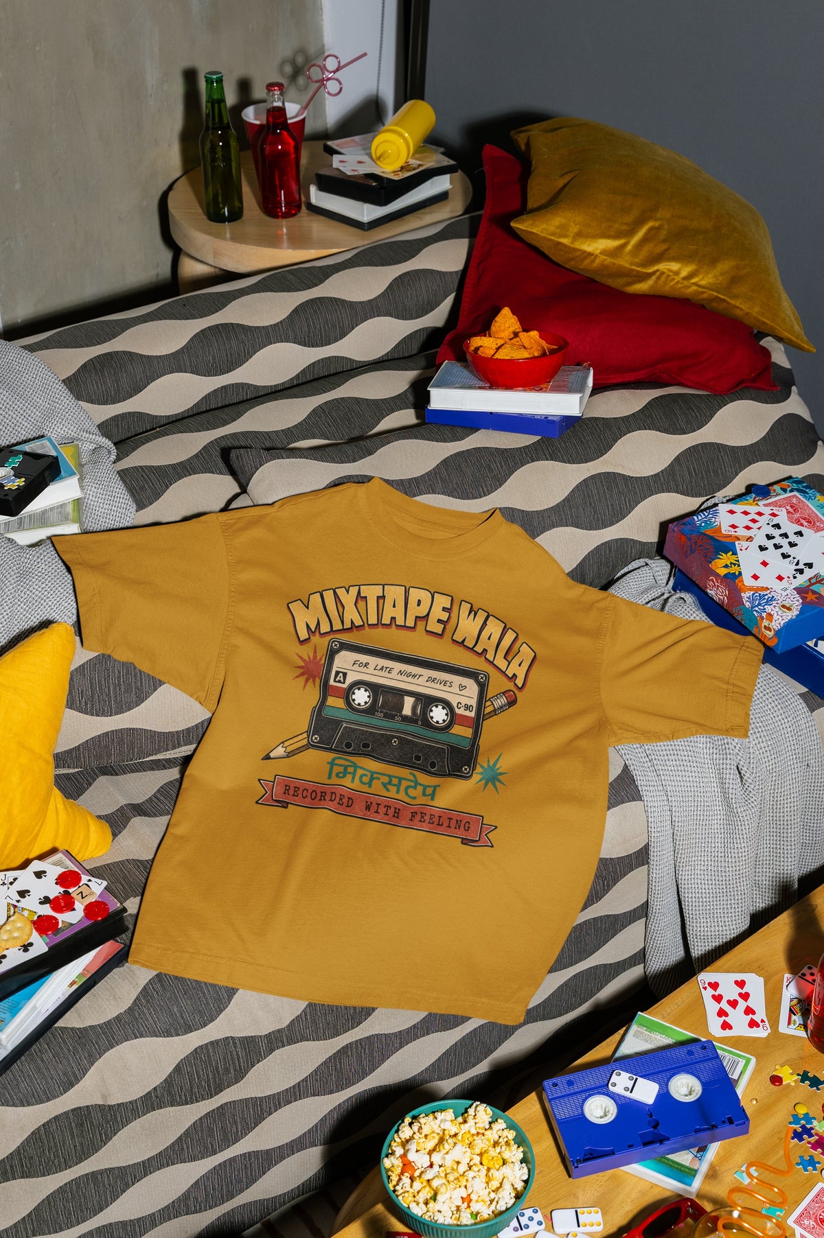 Mustard Yellow Mixtape Wala oversized t-shirt laid flat on a bed with cushions, cassette and popcorn