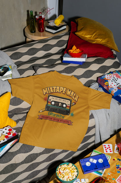 Mustard Yellow Mixtape Wala oversized t-shirt laid flat on a bed with cushions, cassette and popcorn