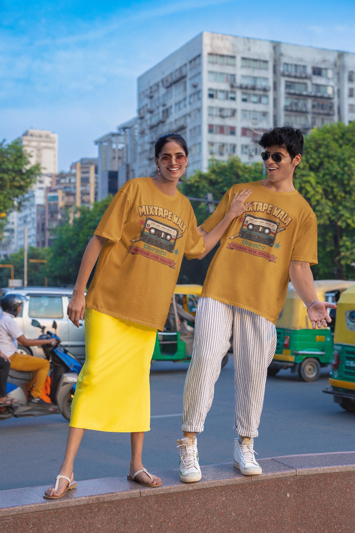 Man and woman wearing the Mustard Yellow Mixtape Wala oversized t-shirt on a city street with auto-rickshaws