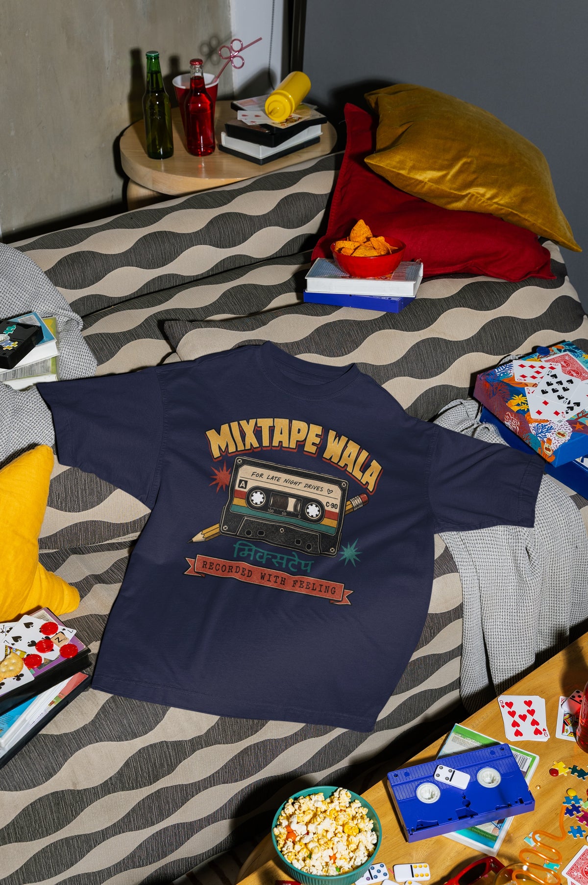 Navy Blue Mixtape Wala oversized t-shirt laid flat on a bed with cushions, cassette and popcorn