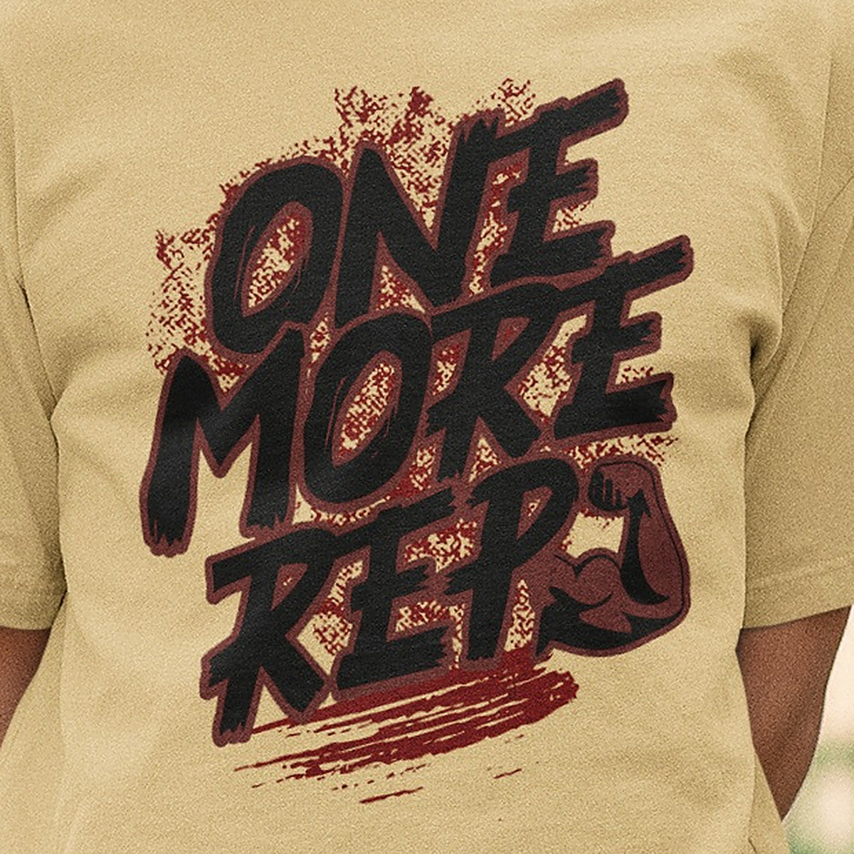 Close-up of the One More Rep brush lettering and flexed arm print on the beige Nauma oversized T-shirt