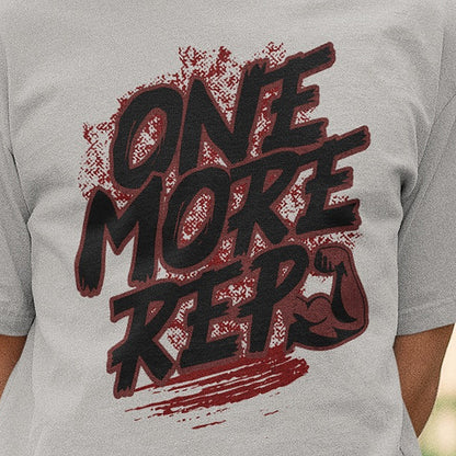 Close-up of the One More Rep brush lettering and flexed arm print on the melange grey Nauma oversized T-shirt