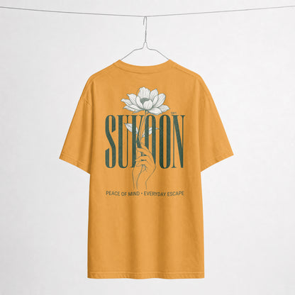 Nauma Sukoon oversized t-shirt in golden yellow on a hanger, back print with lotus flower and hand illustration