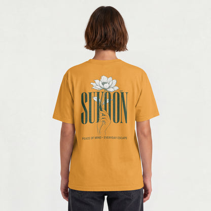 Model wearing Nauma Sukoon oversized t-shirt in golden yellow, back view showing lotus flower and hand print