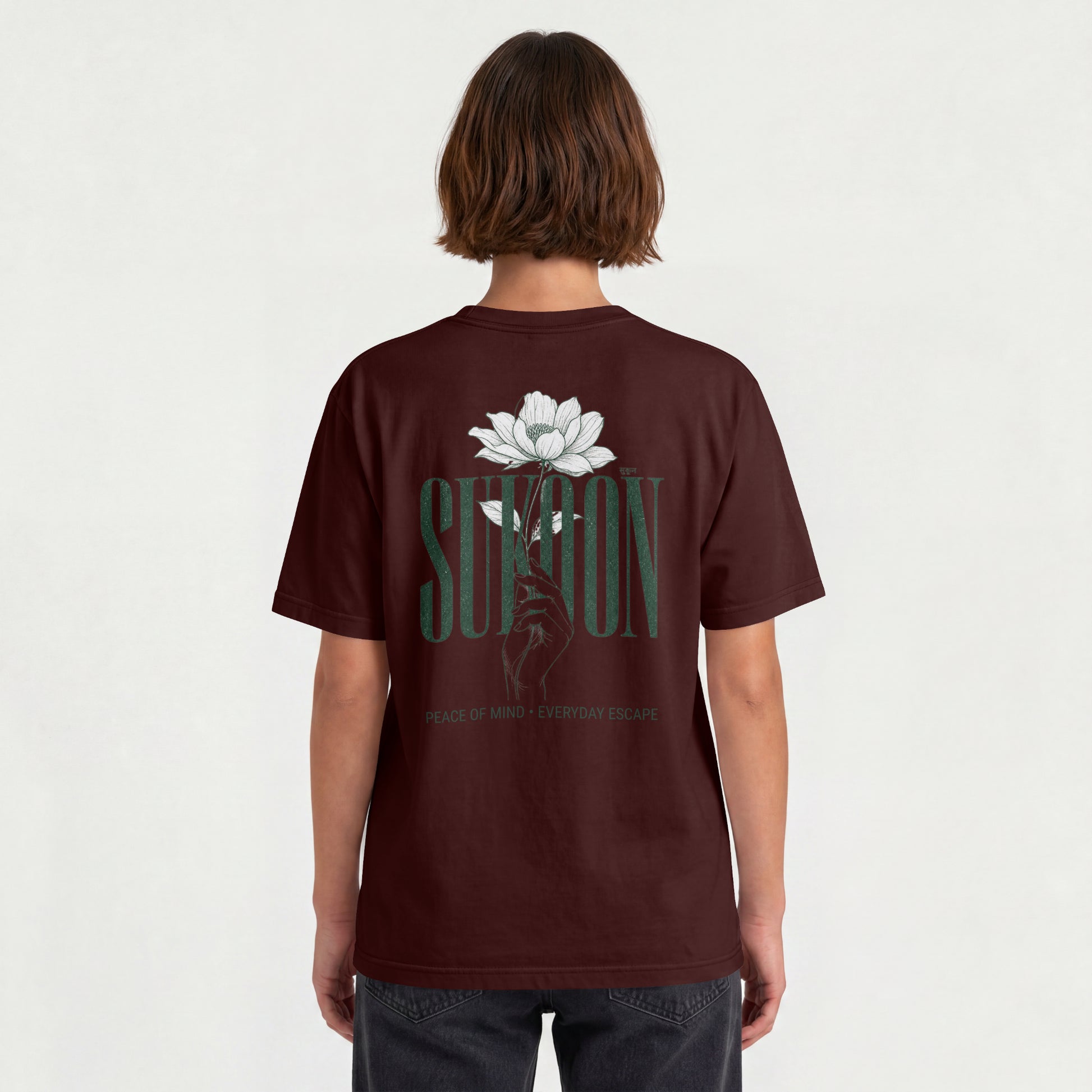 Model wearing Nauma Sukoon oversized t-shirt in maroon, back view showing lotus flower and hand print