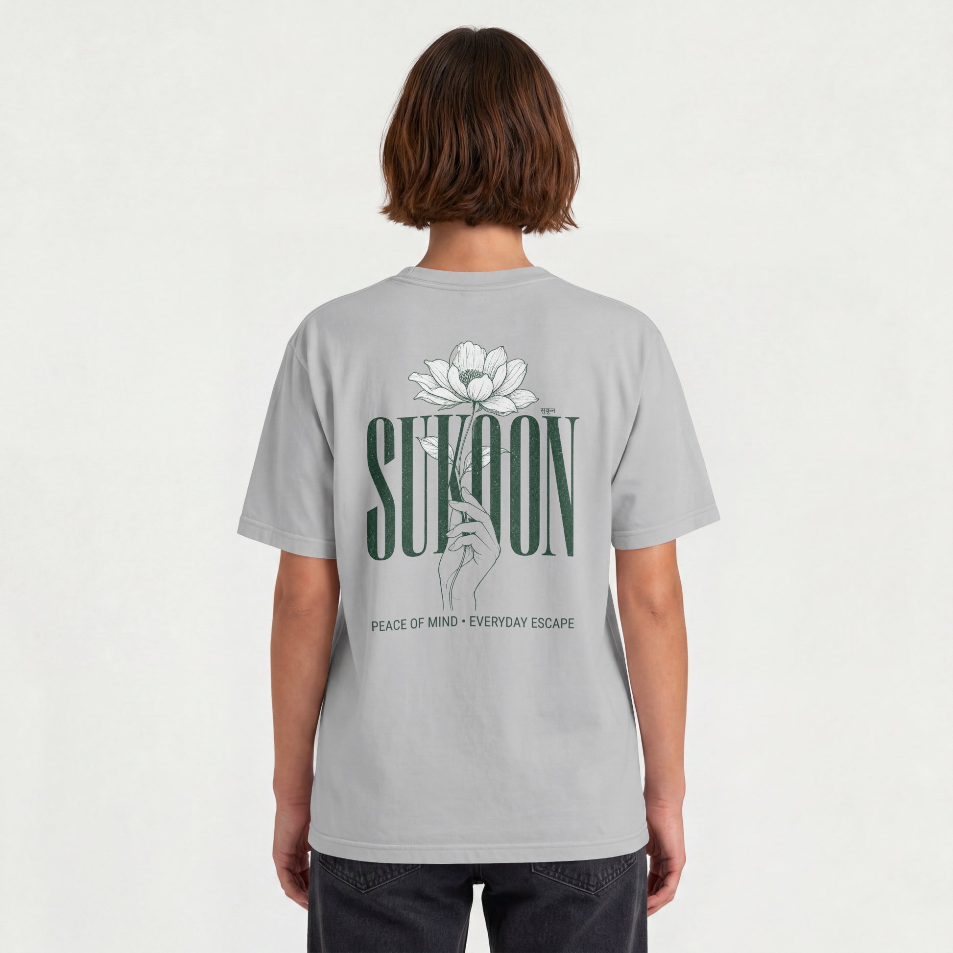 Model wearing Nauma Sukoon oversized t-shirt in melange grey, back view showing lotus flower and hand print