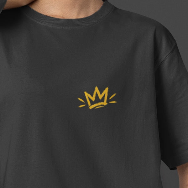 Black Unfortunately Money Is Everything oversized T-shirt front close-up – small mustard yellow crown print on the left chest