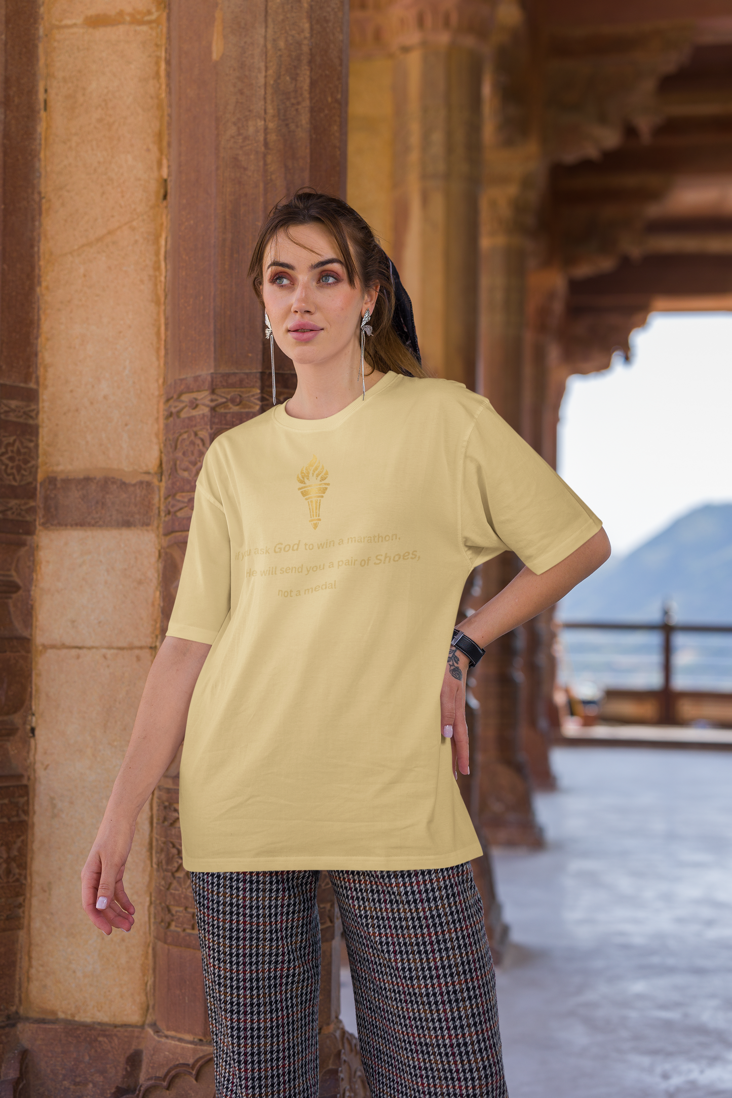 Woman styling a beige baggy-fit drop-shoulder t-shirt with a gold torch print and inspirational message.